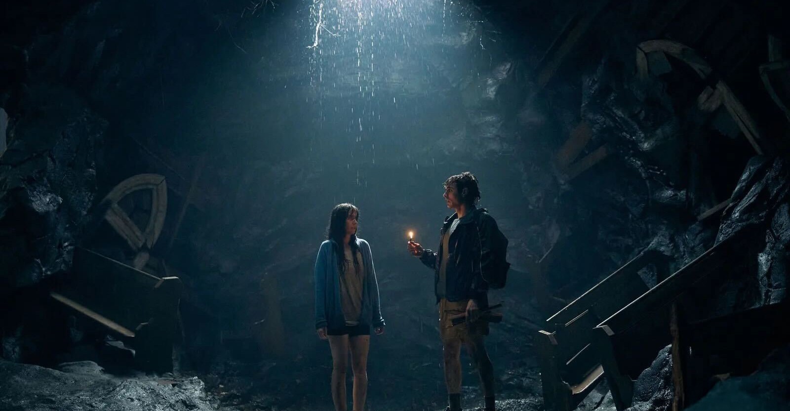 Alison Brie e Dave Franco juntos, em pé em uma caverna escura e úmida enquanto a chuva desce sobre eles de um buraco no teto da caverna acima deles Alison Brie e Dave Franco juntos, em pé em uma caverna escura e úmida enquanto a chuva desce sobre eles de um buraco no teto da caverna acima deles