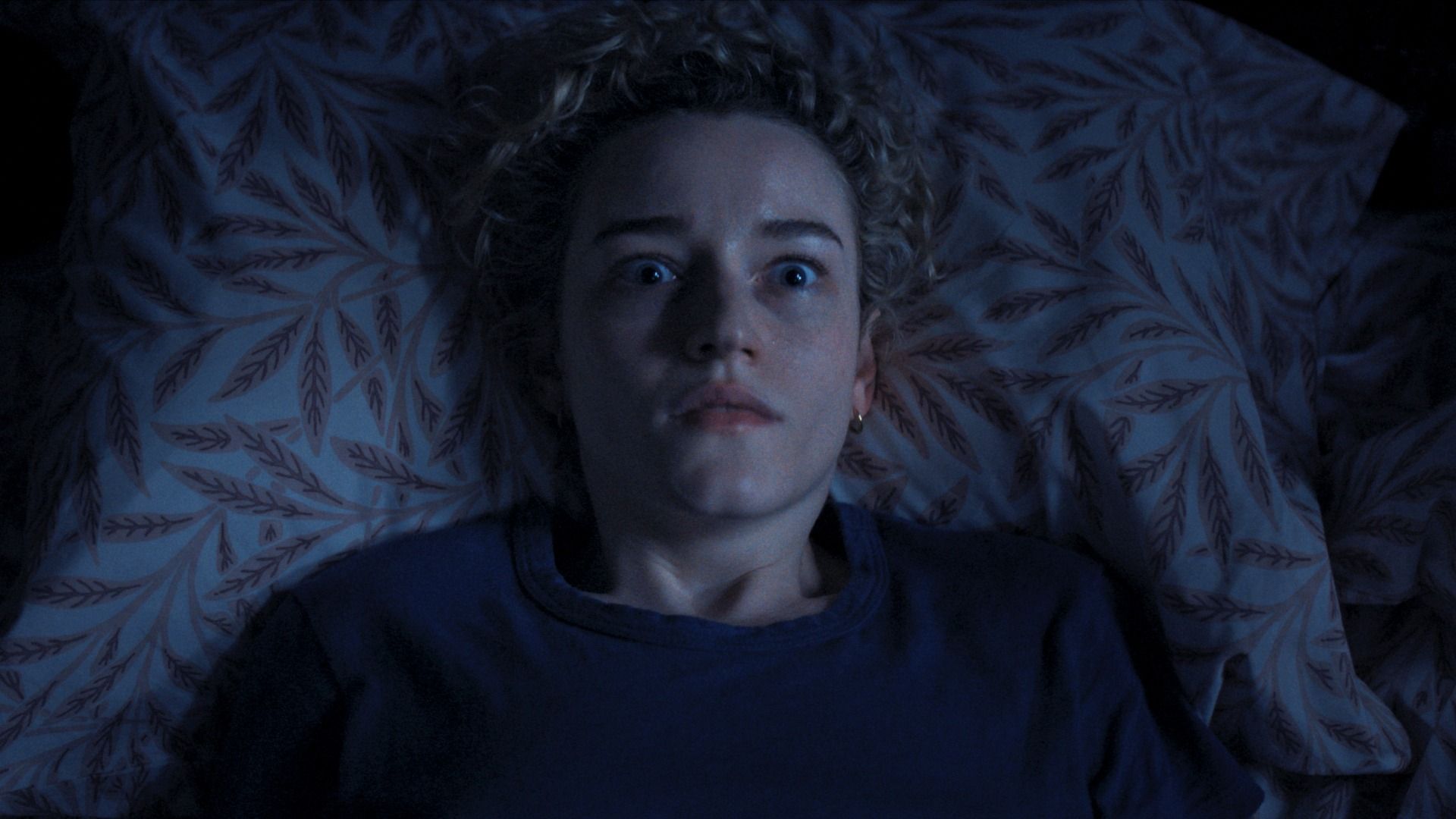 Julia Garner, interpretando uma professora do ensino fundamental cujos alunos desaparecem misteriosamente, acordam na cama em uma cena de armas.