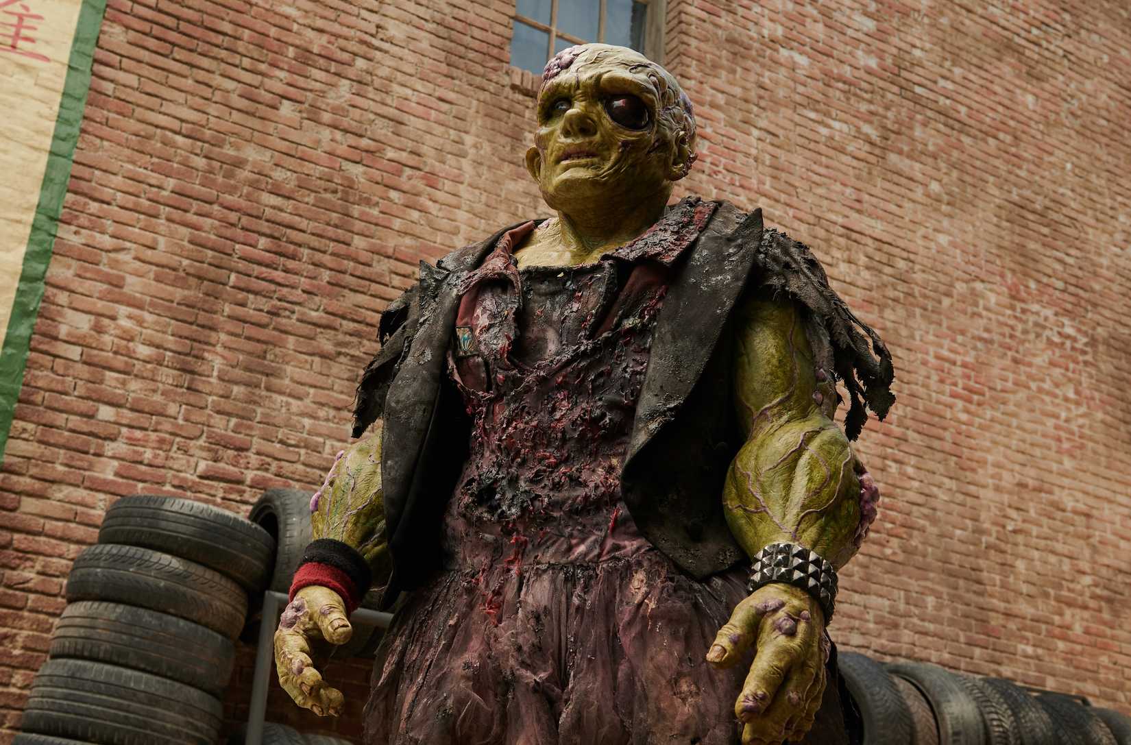 Peter Dinklage como vingador tóxico, um humanóide mutado, de pele verde e com musculação em trapos queimados