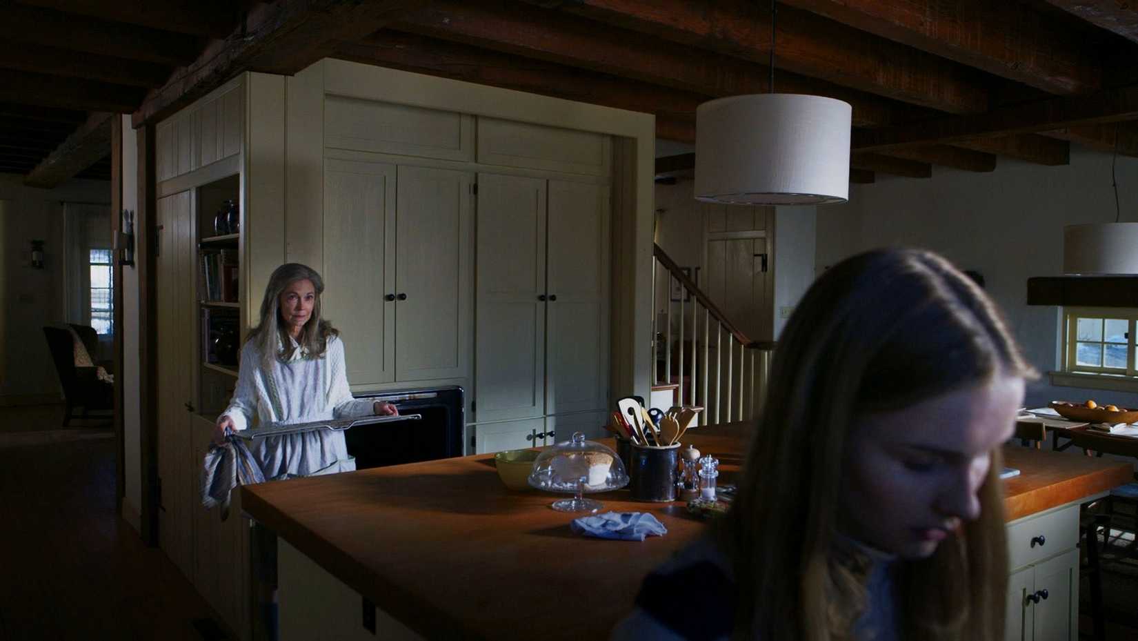 Becca (Olivia Dejonge) fica em primeiro plano de uma cozinha onde sua Nana (Deanna Dunagan) pede que ela limpe o forno em uma cena da visita.