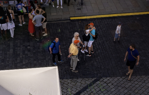 Um homem e uma mulher, cercados por outras pessoas, beijam em uma rua no meio de um evento.