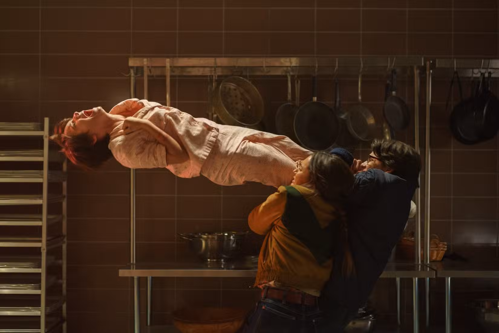 Gwen (Madeleine McGraw), de pijama rosa, flutua de costas no ar, gritando e apertando a garganta, enquanto várias pessoas se agarram às suas pernas e tentam puxá-la para baixo em Black Phone 2