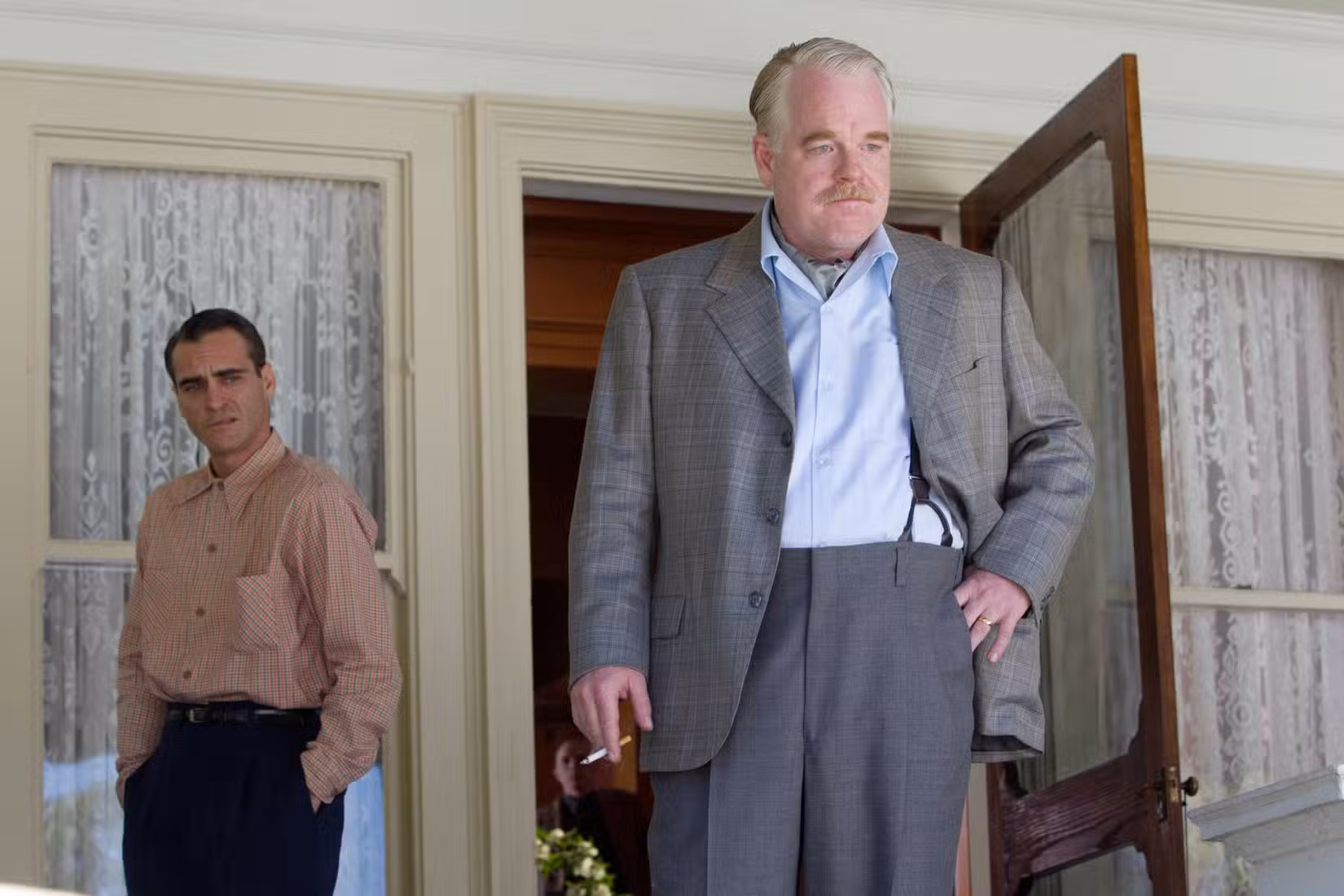 Philip Seymour Hoffman como Lancaster Dodd fuma um cigarro na varanda enquanto Freddie observa em The MasterJoaquin Phoenix's 