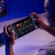 Um homem joga um ROG Xbox Ally X em uma mesa com um monitor e teclado em segundo plano