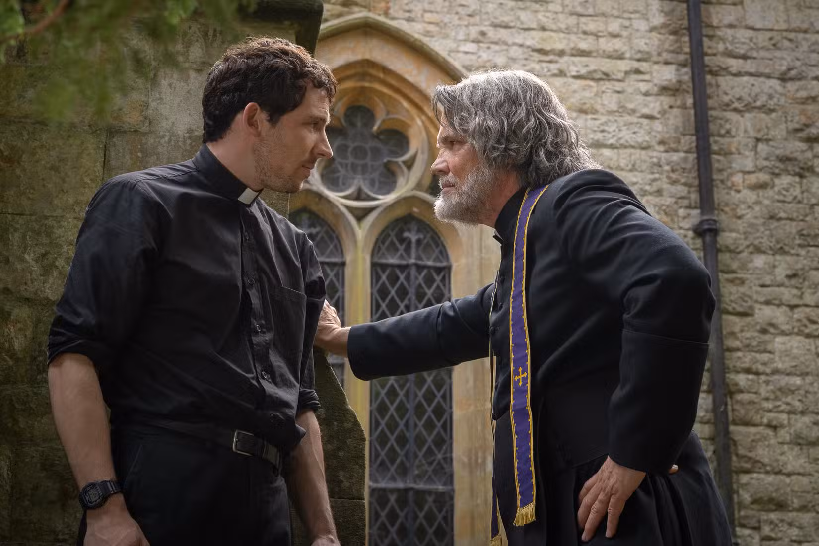 Josh O'Connor e Josh Brolin, vestidos como padres, ficam confrontativamente próximos um do outro em Wake Up Dead Man: A Knives Out Mystery