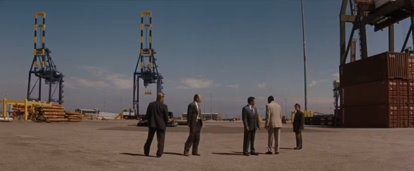 Em uma cena do filme Heat, um grupo de policiais liderados por Vincent Hanna (Al Pacino), visto de uma perspectiva ampla, examina uma área industrial em busca de sinais de atividade criminosa.