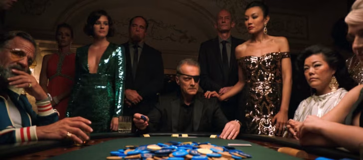 Um homem de aparência severa e tapa-olho está sentado em uma mesa de pôquer em Las Vegas, cercado por espectadores sérios, no episódio 6 de Pluribus
