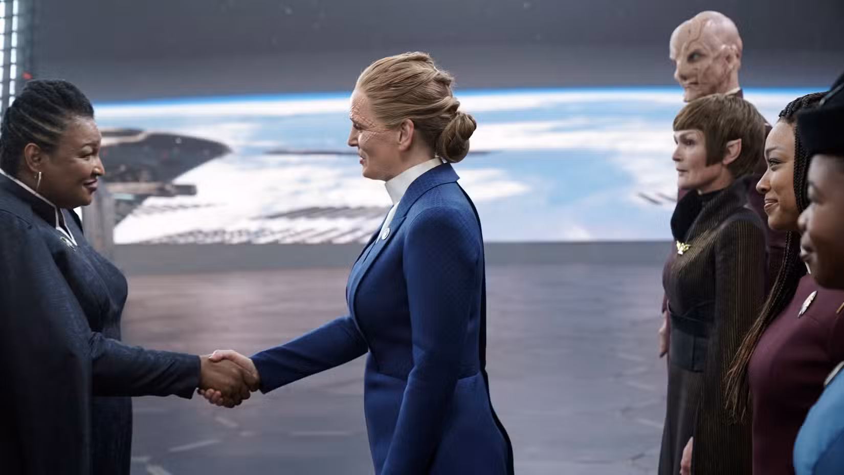 O Presidente da Terra Unida (Stacey Abrams) aperta a mão do Presidente da Federação Rillak (Chelah Horsal) enquanto a tripulação do Discovery assiste Star Trek: Discovery