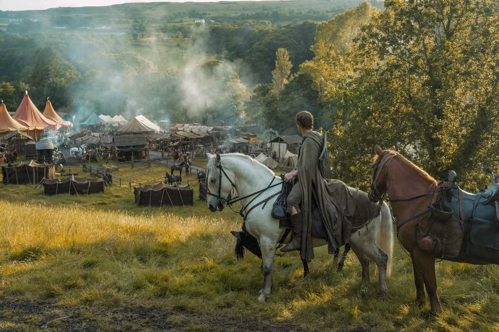 Dunk (Peter Claffey), um homem alto com uma longa capa verde, está sentado a cavalo em uma colina acima de uma pequena cidade medieval no spin-off de Game of Thrones, Um Cavaleiro dos Sete Reinos.