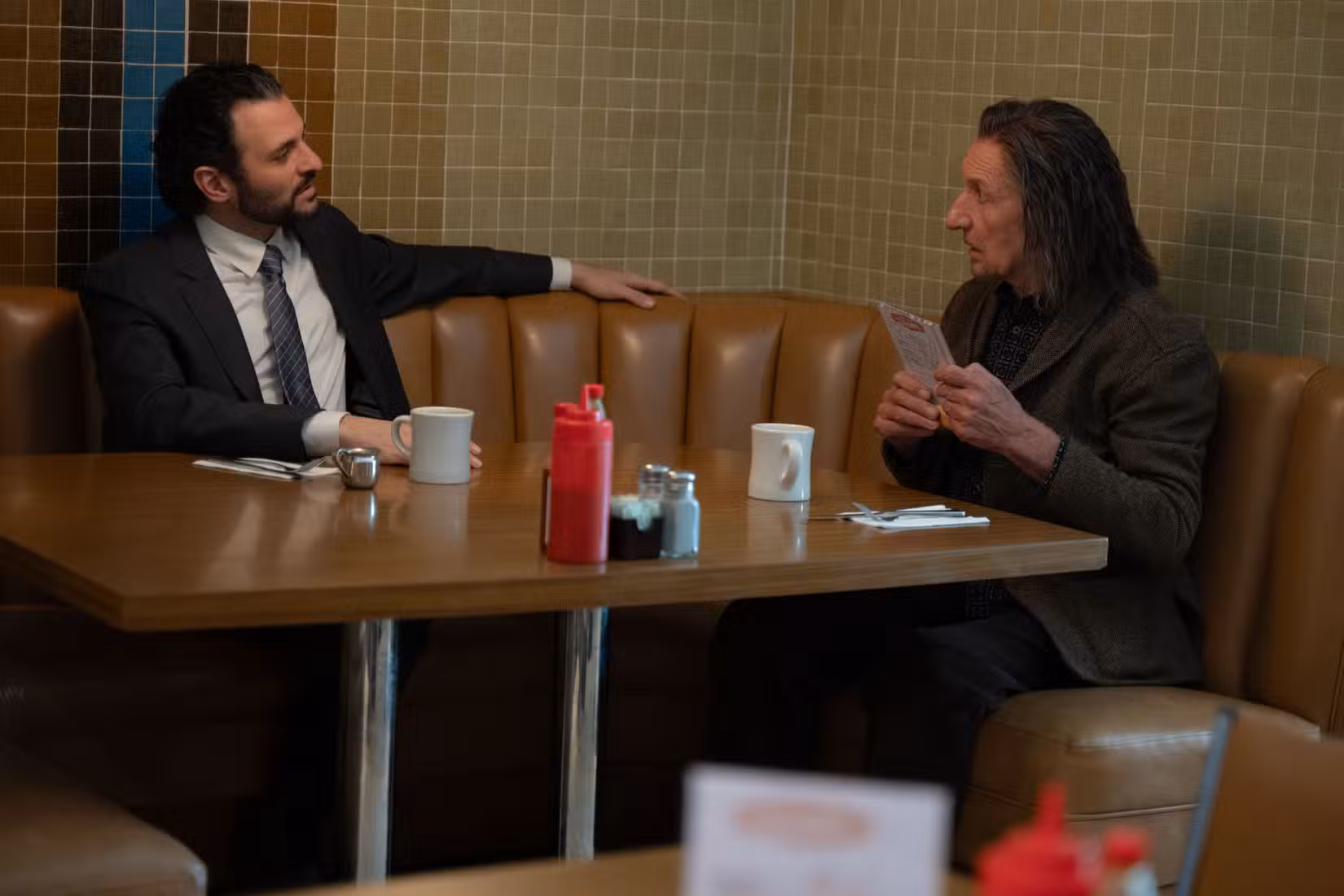 O agente Cleary (Arian Moayed) está sentado em uma lanchonete com Trevor Slattery (Ben Kingsley) em Wonder Man