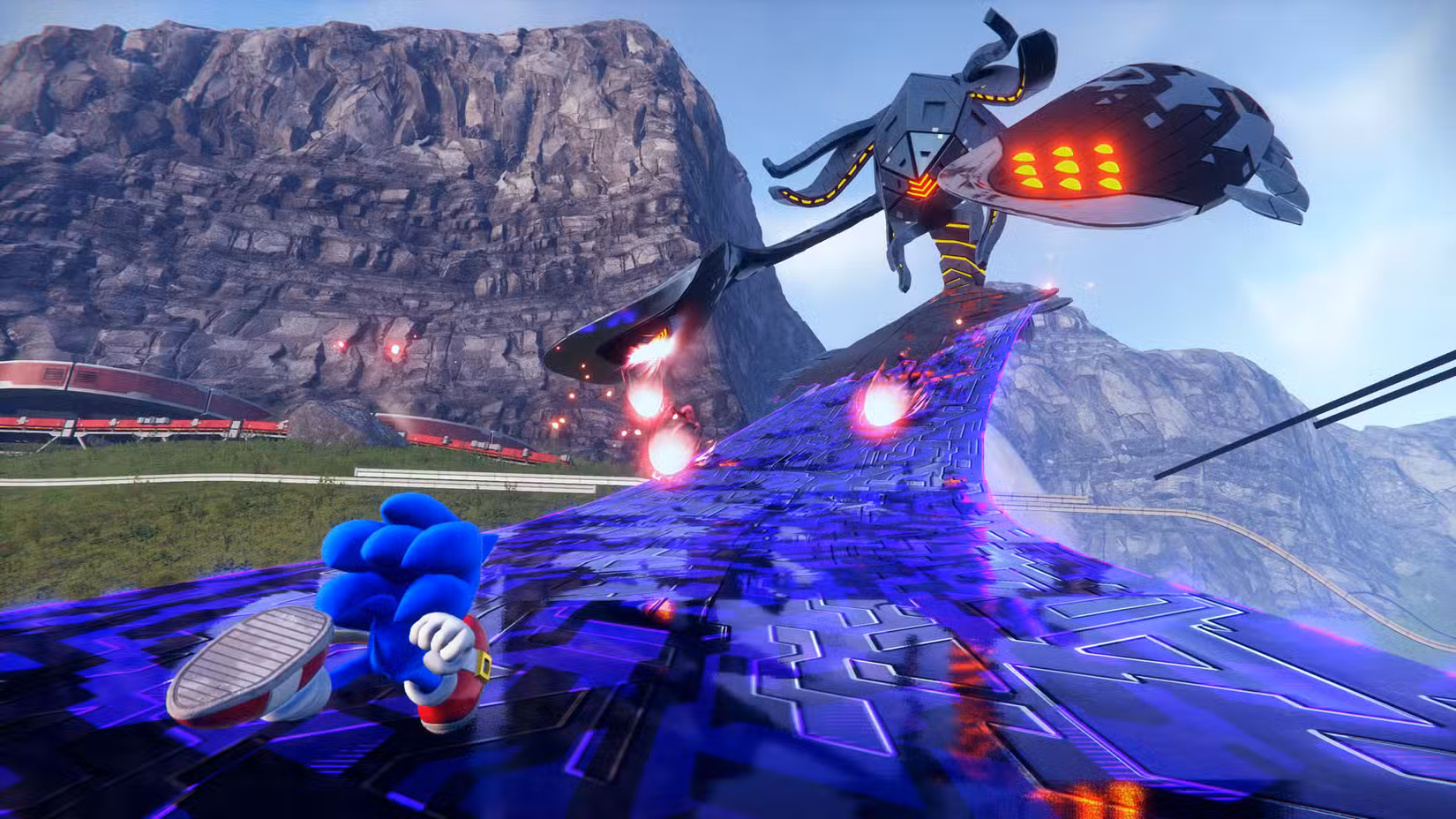 Sonic the Hedgehog corre pelo membro elegante de uma criatura gigante de metal com um olho só chamada Titã em uma área de mundo aberto cercada por uma cordilheira em uma captura de tela de Sonic Frontiers