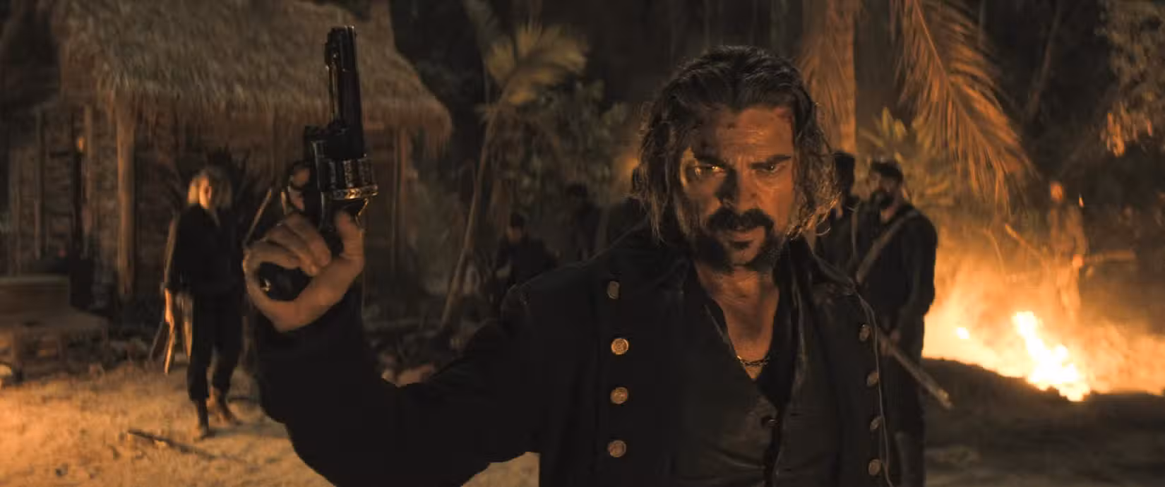 Karl Urban, interpretando um pirata assassino, brande uma pistola em close-up médio em frente a uma fogueira noturna em uma cena de The Bluff