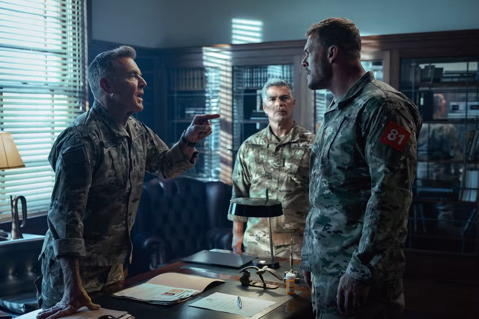 Dois oficiais do Exército (Dennis Quaid, Esai Morales) repreendem o sargento 81 (Alan Ritchson) em um escritório militar em War Machine