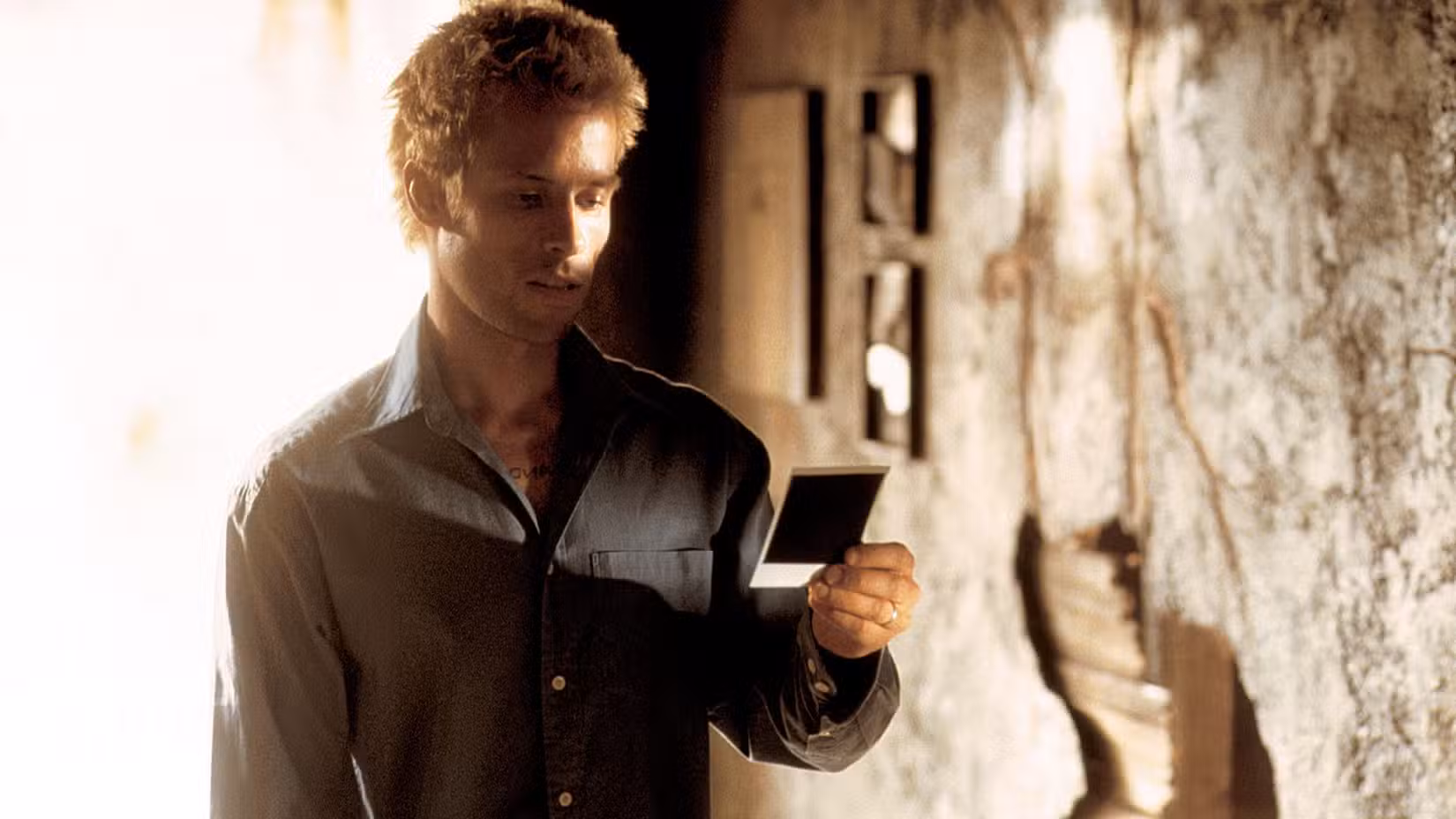 Leonard Shelby (Guy Peace), está em um prédio desgastado segurando uma foto Polaroid em Memento.