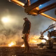 O diretor Patrick Hughes durante a produção de War Machine, em um campo noturno cercado por fogo e equipamentos de câmera