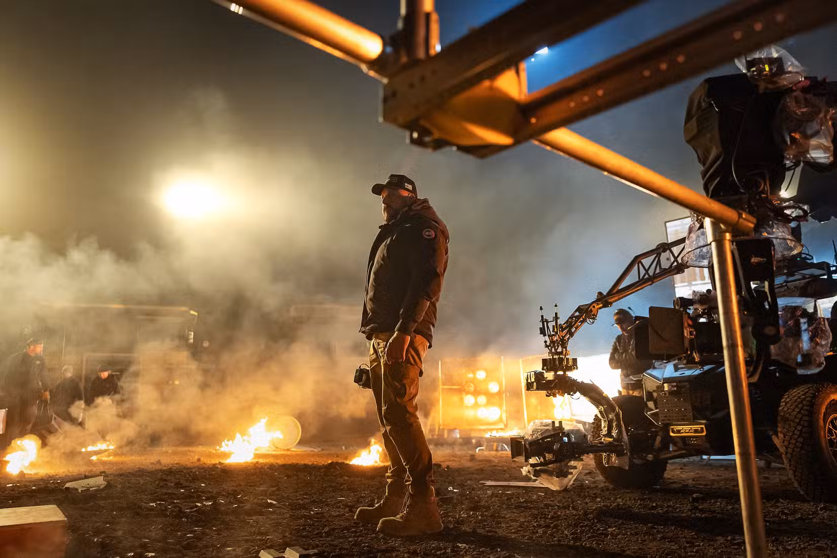 O diretor Patrick Hughes durante a produção de War Machine, em um campo noturno cercado por fogo e equipamentos de câmera