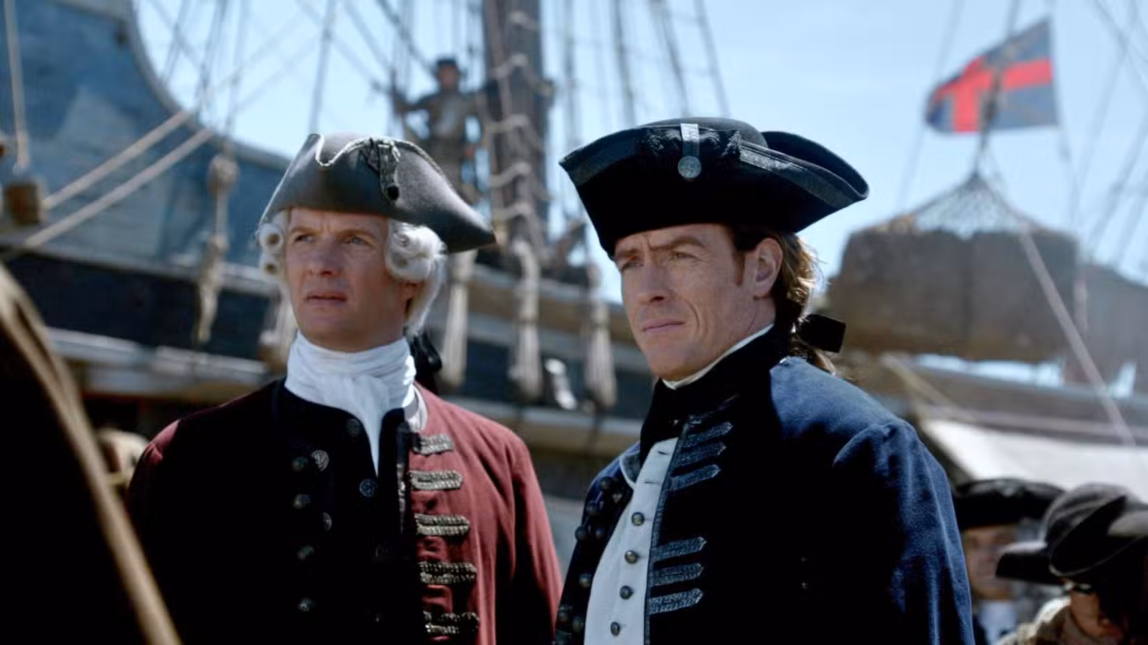 Thomas Hamilton, usando um chapéu tricórnio e um casaco vermelho, está ao lado do capitão Flint, que também usa a mesma roupa, mas seu casaco é azul para indicar sua posição como oficial da Marinha Real.