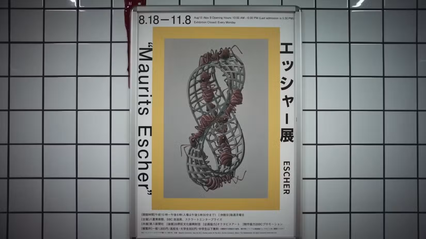 Uma captura de tela do trailer da Saída 8 mostrando um dos pôsteres no corredor, uma impressão de Escher com texto e uma tira de Moebius com formigas andando sobre ela