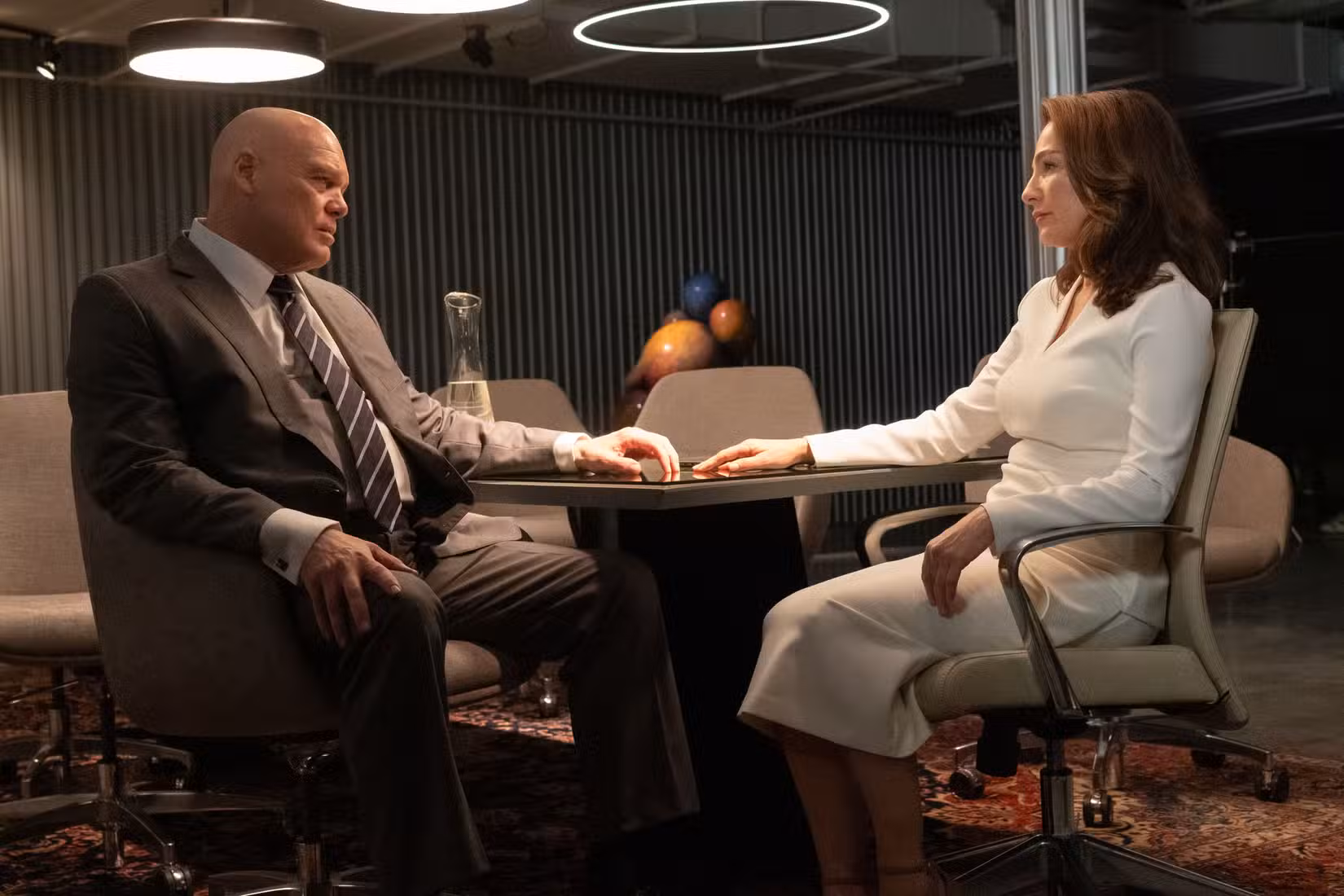 Kingpin e Vanessa estão sentados a uma mesa, olhando um para o outro, com as mãos estendidas sobre a mesa e quase se tocando, em Demolidor: Nascido de Novo