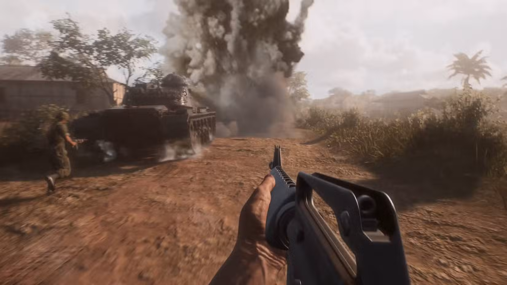 Um soldado em Hell Let Loose: Vietnam em pé com um rifle de assalto ao lado de um tanque com uma explosão na frente dele.