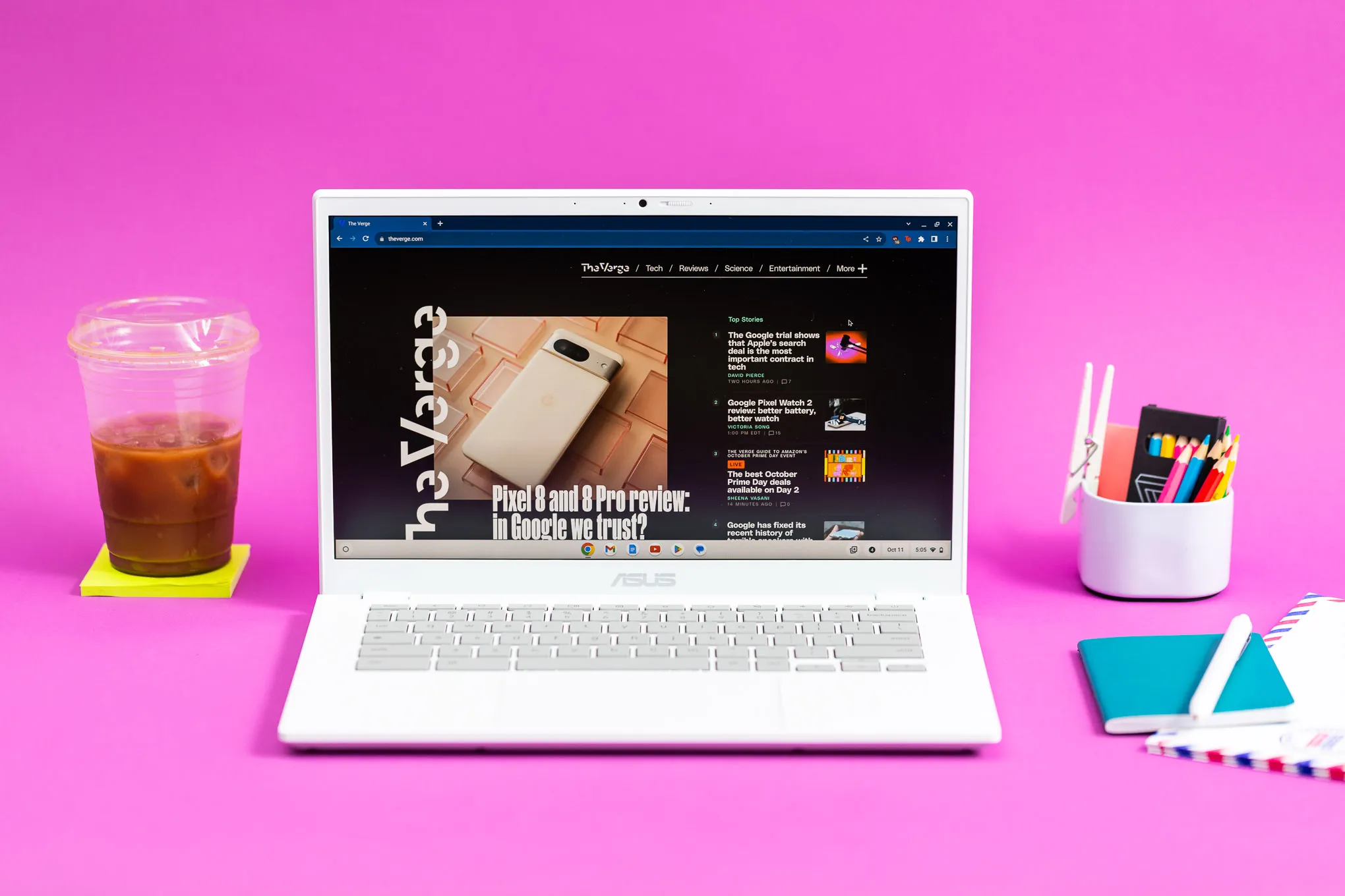 The Asus Chromebook Plus CX34 displaying The Verge homepage between an iced coffee and a cup of colored pencils.