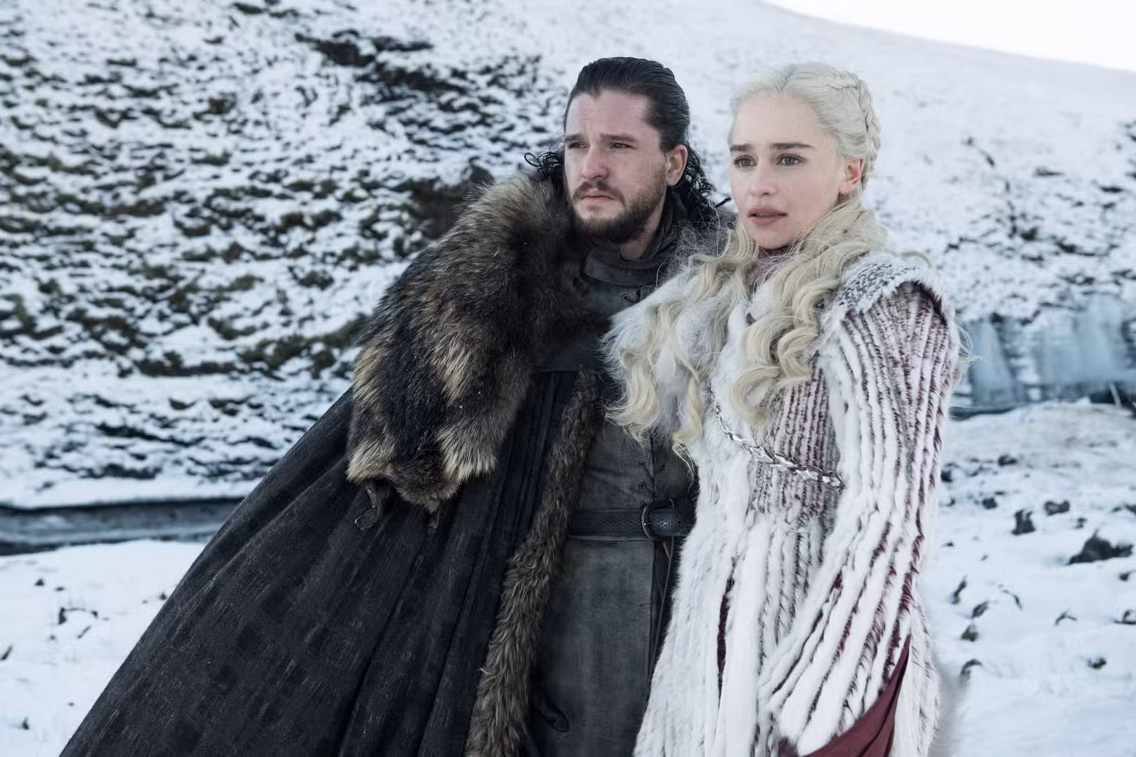 Kit Harington e Emilia Clarke como Jon Snow e Daenerys Targaryen em Game of Thrones. Eles estão em um campo de neve, vestidos com peles. 