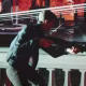 James Bond segura uma espingarda em uma sala iluminada em vermelho enquanto balas passam