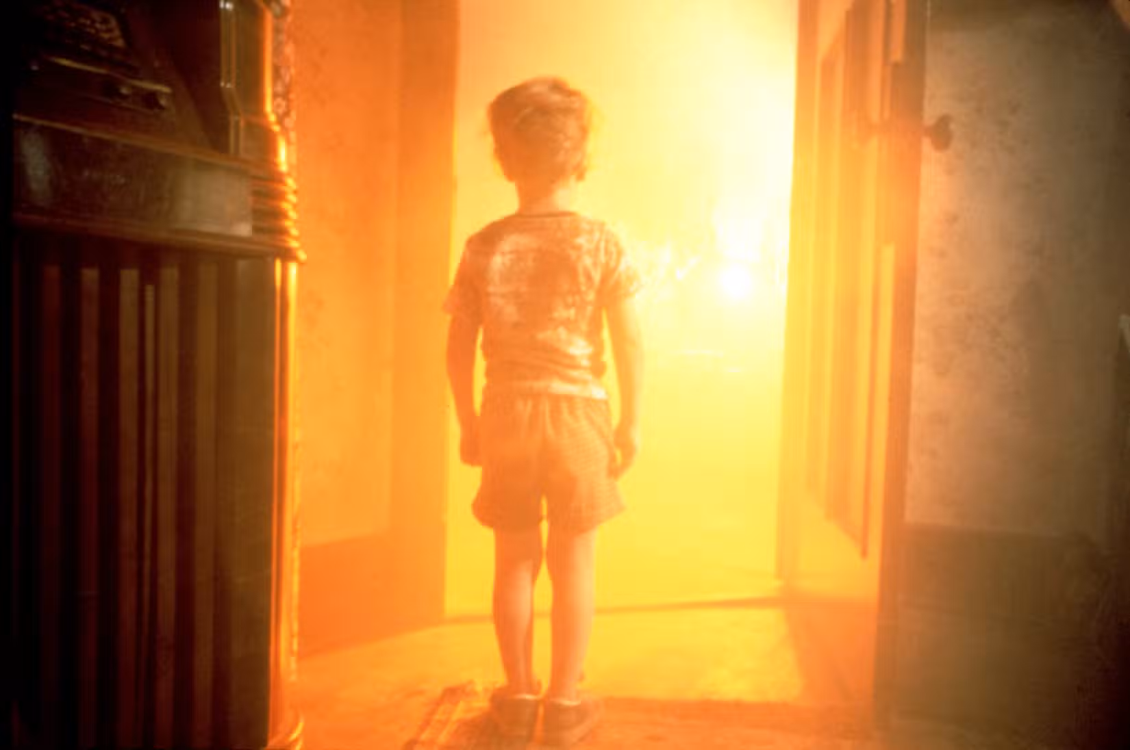 A small boy stands in front of a bright yellow light