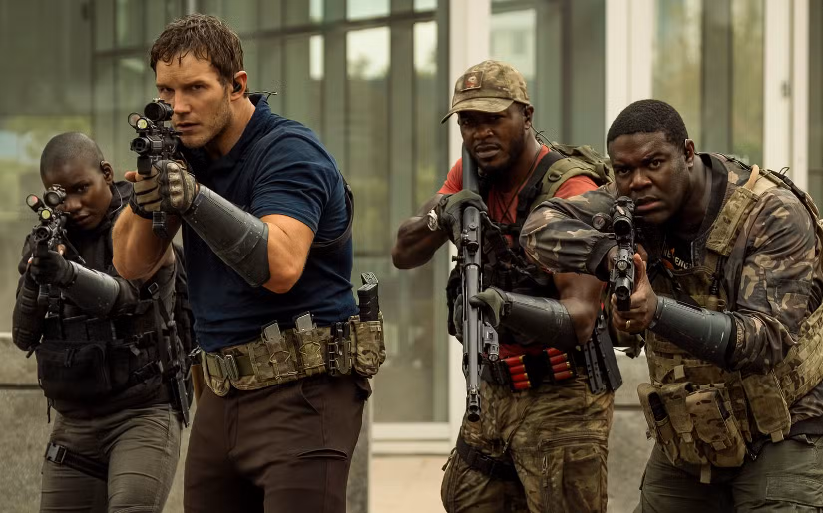 Chris Pratt stands meaningfully at the head of a small group of armed and camo-wearing soldiers, all of whom are Black except him
