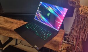 A Razer Blade 16 gaming laptop in front of a TV next to a wooden sculpture