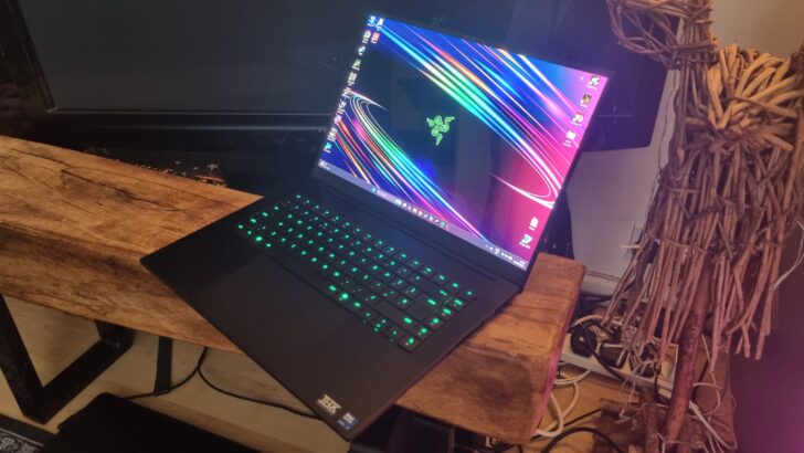 A Razer Blade 16 gaming laptop in front of a TV next to a wooden sculpture