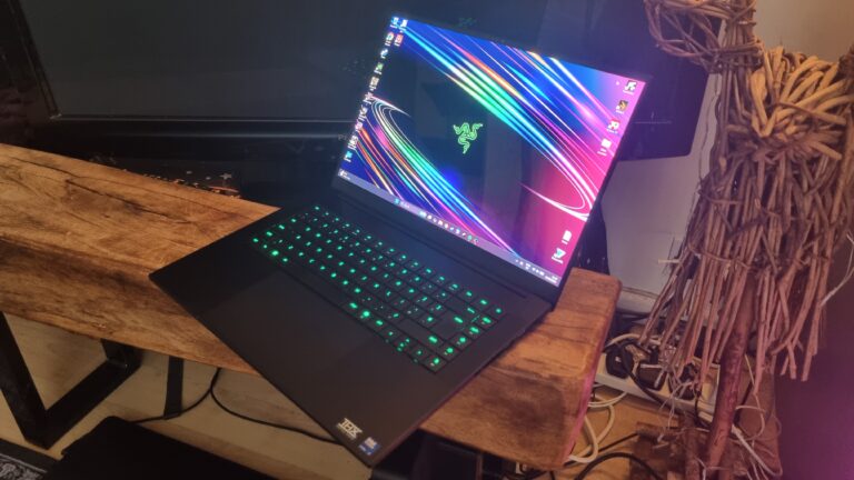 A Razer Blade 16 gaming laptop in front of a TV next to a wooden sculpture
